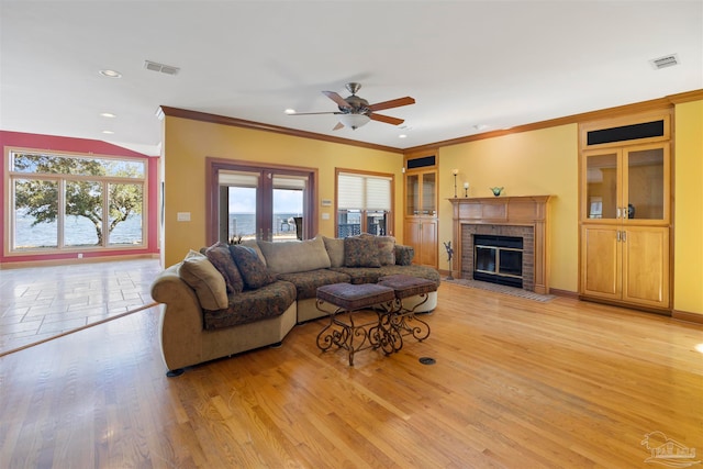 living room with ornamental molding, a fireplace, light wood-type flooring, and ceiling fan