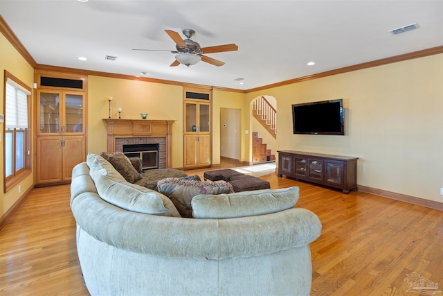 living room with crown molding, a fireplace, light wood-type flooring, and ceiling fan