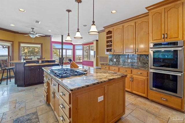 kitchen with tasteful backsplash, light stone countertops, appliances with stainless steel finishes, a center island, and hanging light fixtures