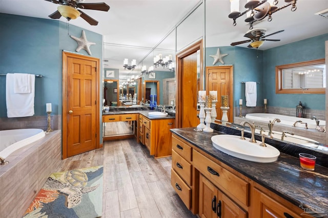 bathroom featuring vanity, wood-type flooring, ceiling fan with notable chandelier, and tiled bath