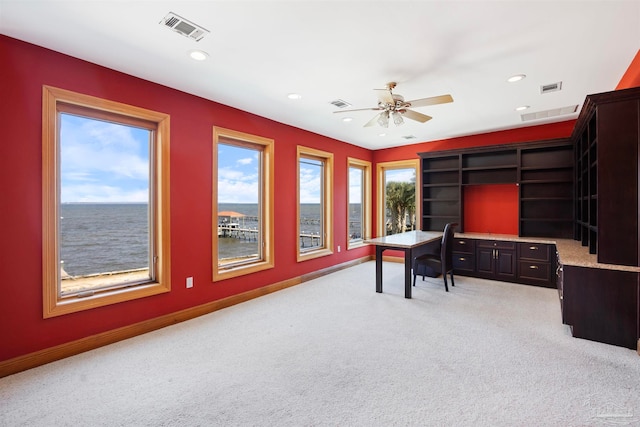 home office featuring a water view, light carpet, and ceiling fan