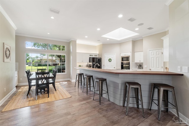 4282 Walden Way, Gulf Breeze, FL 32563 - kitchen featuring black refrigerator with ice dispenser, wall oven, stainless steel microwave, a skylight, and a breakfast bar area