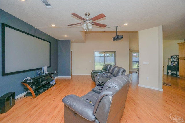 cinema room with light wood-type flooring, ceiling fan, and a textured ceiling