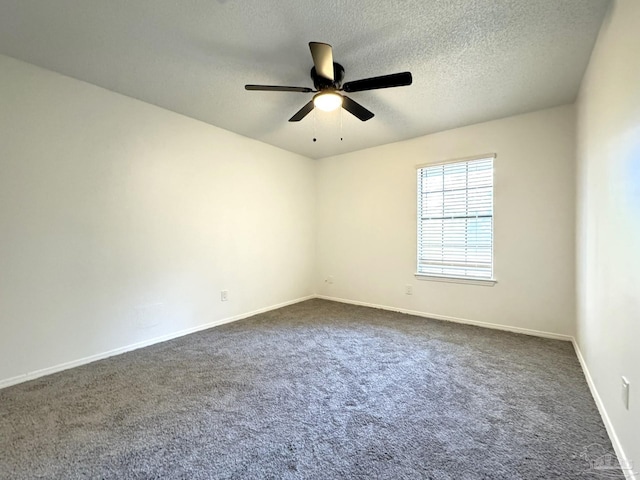 spare room featuring a textured ceiling, dark carpet, and ceiling fan