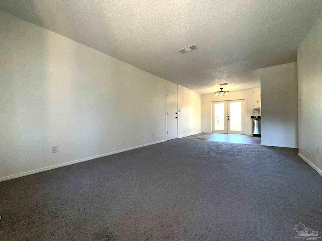 unfurnished living room with a notable chandelier, dark carpet, a textured ceiling, and french doors