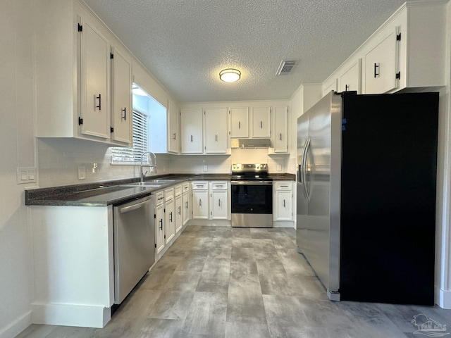 kitchen with light wood-type flooring, a textured ceiling, stainless steel appliances, sink, and white cabinets