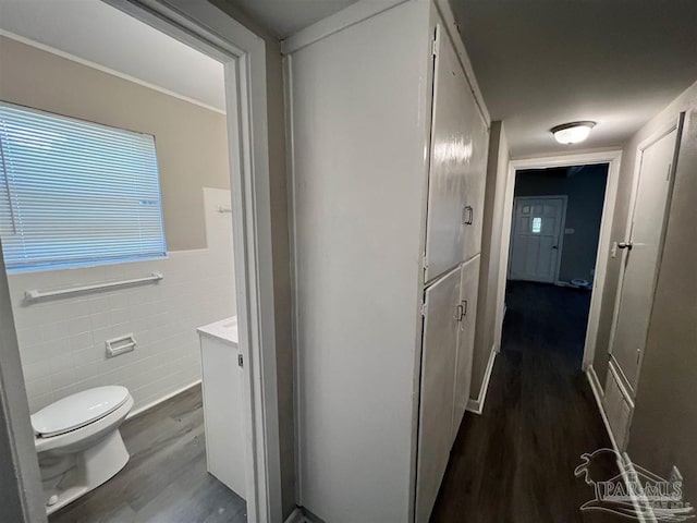 hall featuring dark wood-style flooring, wainscoting, and tile walls