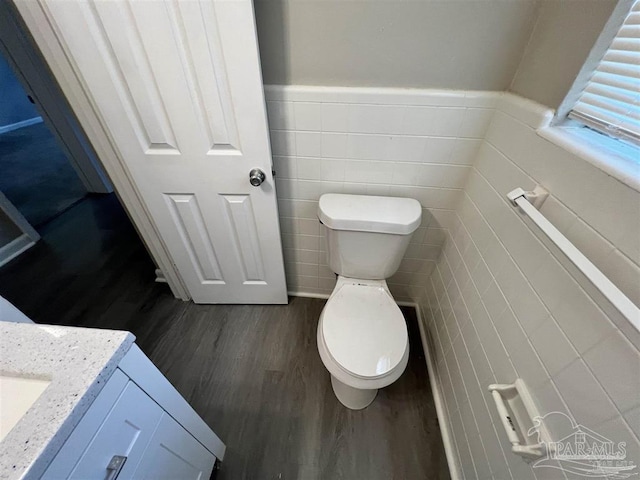 bathroom with tile walls, toilet, wainscoting, vanity, and wood finished floors