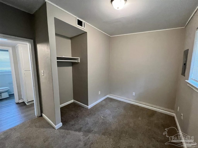 unfurnished bedroom featuring baseboards, visible vents, ornamental molding, dark carpet, and a closet