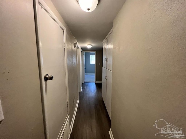 corridor with dark wood-style flooring and baseboards