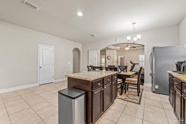 kitchen featuring dark brown cabinetry, hanging light fixtures, a center island, and stainless steel refrigerator