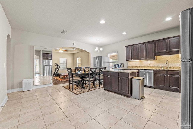 kitchen featuring appliances with stainless steel finishes, pendant lighting, decorative backsplash, light tile patterned floors, and dark brown cabinets