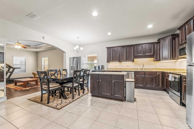 kitchen with light tile patterned flooring, dark brown cabinetry, pendant lighting, stainless steel appliances, and light stone countertops