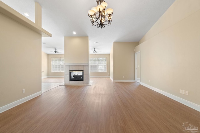 unfurnished living room with wood-type flooring, ceiling fan with notable chandelier, and a fireplace