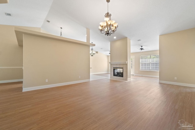 unfurnished living room with a tiled fireplace, ceiling fan with notable chandelier, and light hardwood / wood-style floors