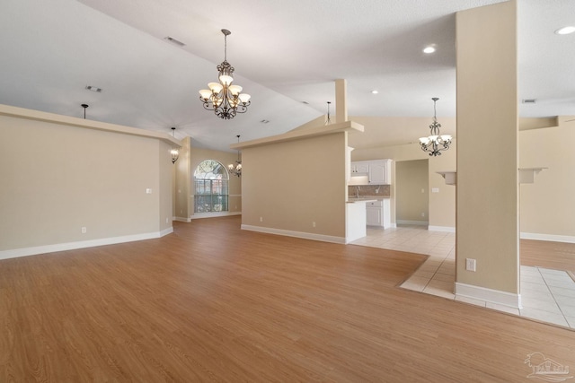 unfurnished living room with a notable chandelier, light hardwood / wood-style flooring, and vaulted ceiling