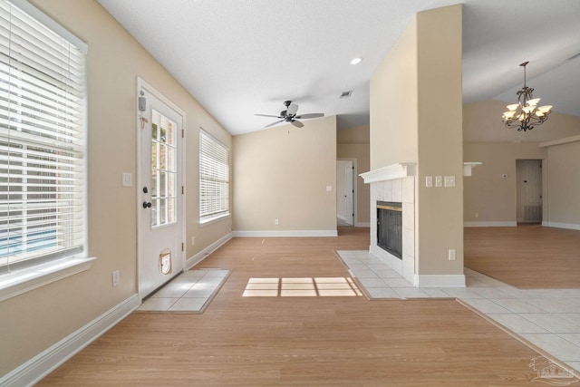 unfurnished living room featuring lofted ceiling, light tile patterned floors, a fireplace, a textured ceiling, and ceiling fan with notable chandelier