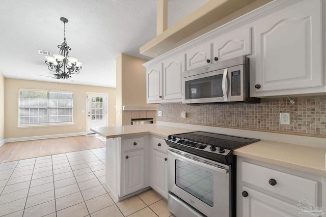 kitchen with hanging light fixtures, kitchen peninsula, stainless steel appliances, decorative backsplash, and white cabinets