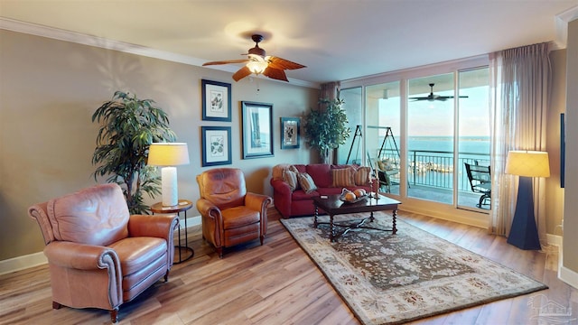 living area with ornamental molding, light wood-style floors, baseboards, and a ceiling fan