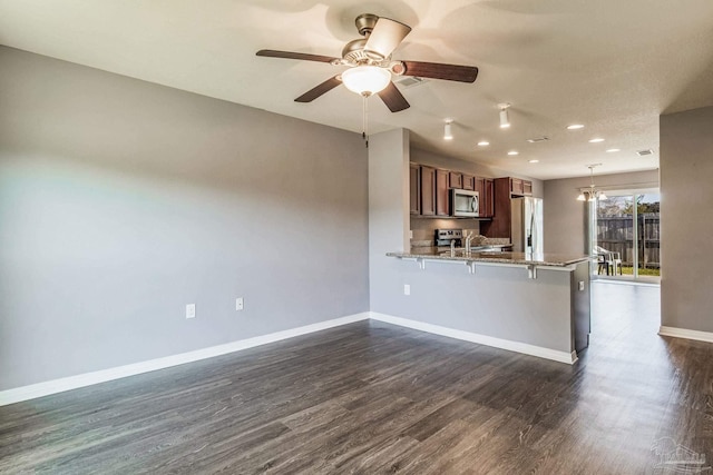 kitchen featuring kitchen peninsula, appliances with stainless steel finishes, a breakfast bar, sink, and dark hardwood / wood-style floors