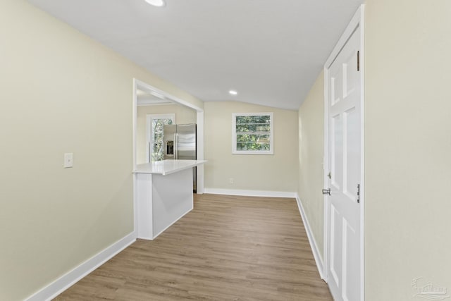 corridor with light hardwood / wood-style floors and lofted ceiling