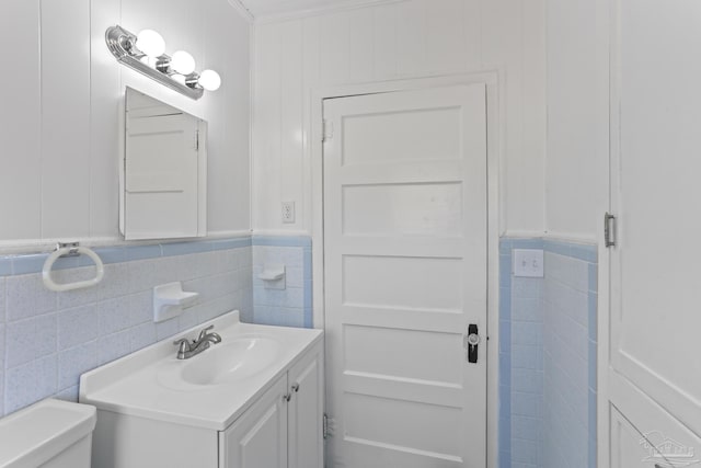 bathroom with crown molding, vanity, tile walls, and toilet