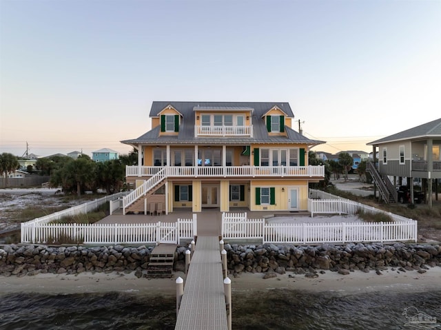 back house at dusk featuring a balcony and a water view