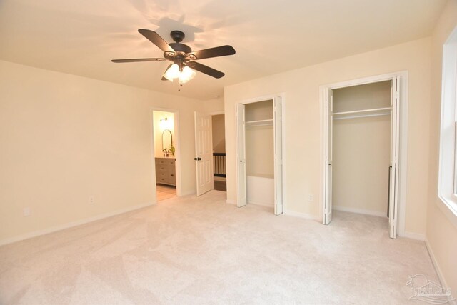 unfurnished bedroom with ceiling fan, multiple closets, connected bathroom, and light carpet