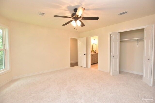 unfurnished bedroom featuring light carpet, ceiling fan, ensuite bathroom, and a closet