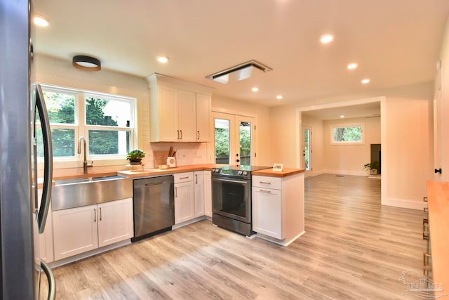 kitchen featuring butcher block countertops, stainless steel appliances, plenty of natural light, and white cabinetry