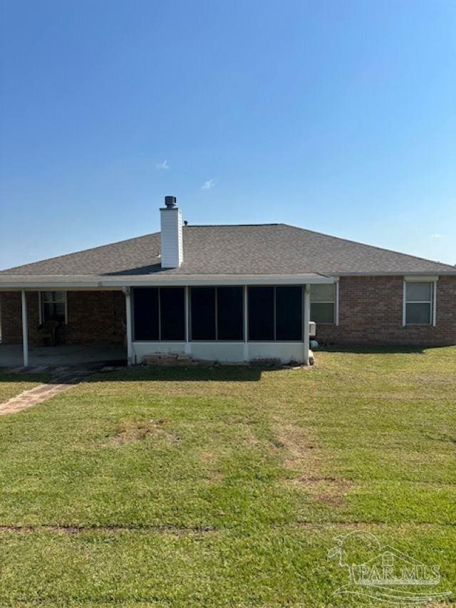 rear view of property with brick siding, a shingled roof, a sunroom, a yard, and a chimney