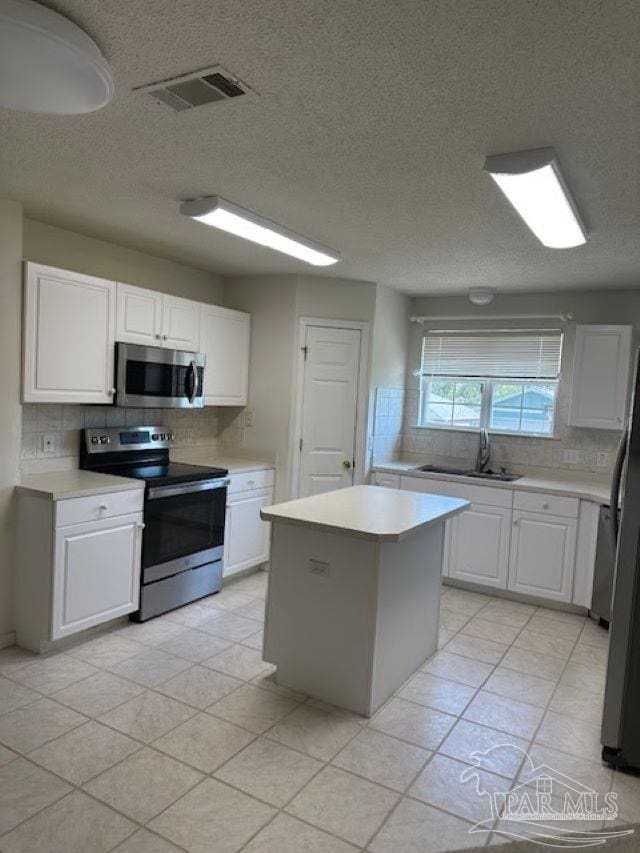 kitchen featuring light countertops, backsplash, appliances with stainless steel finishes, white cabinetry, and a sink