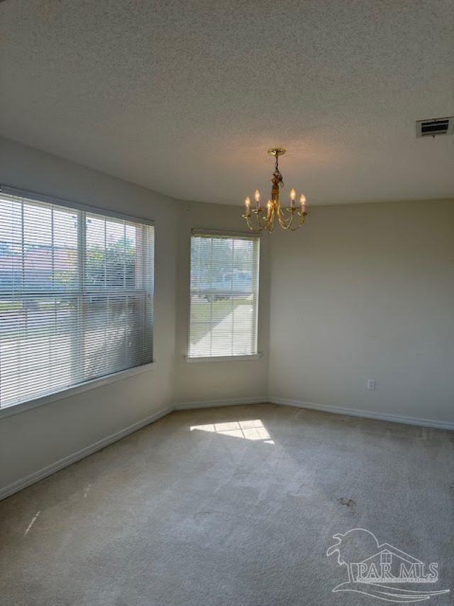 spare room with carpet, visible vents, a textured ceiling, and an inviting chandelier