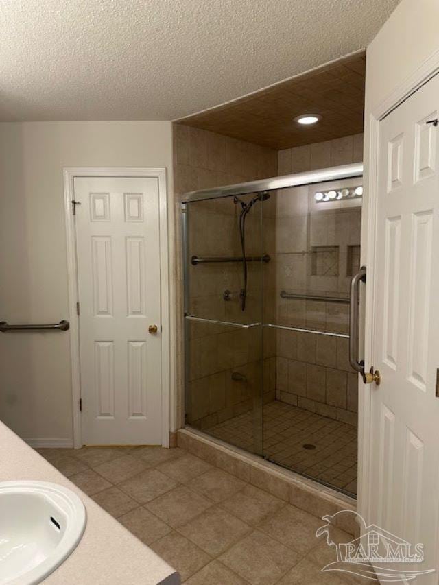 bathroom featuring a textured ceiling, a sink, a shower stall, and tile patterned floors