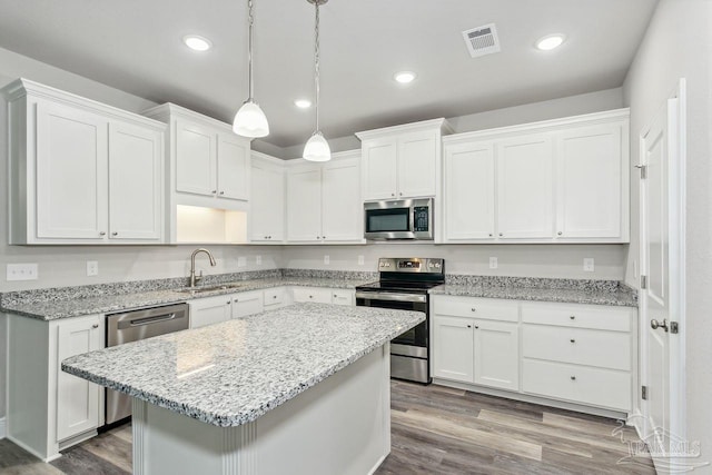 kitchen featuring sink, hanging light fixtures, stainless steel appliances, light hardwood / wood-style floors, and white cabinets