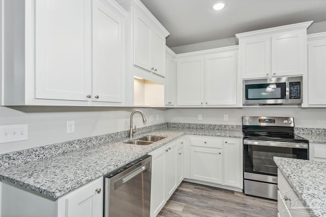 kitchen with stainless steel appliances, white cabinetry, sink, and hardwood / wood-style floors