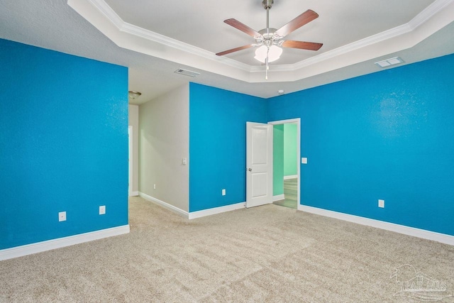 spare room with ceiling fan, light colored carpet, ornamental molding, and a raised ceiling