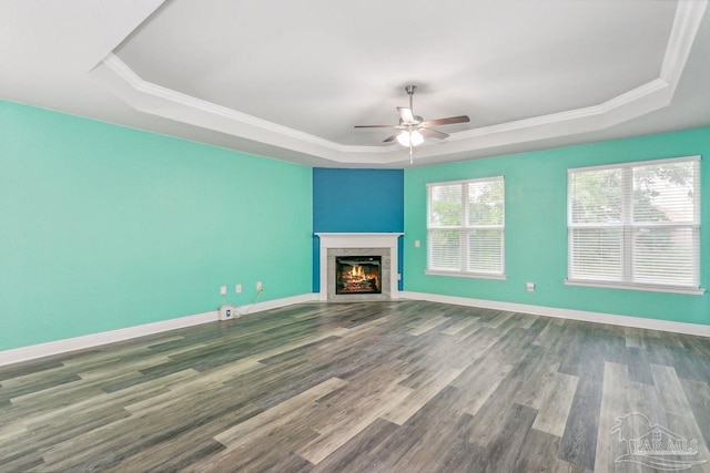 unfurnished living room featuring crown molding, a raised ceiling, a tile fireplace, hardwood / wood-style flooring, and ceiling fan