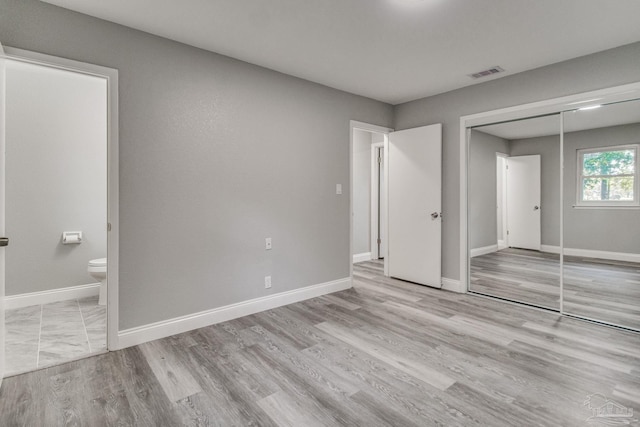 unfurnished bedroom featuring ensuite bathroom, light hardwood / wood-style flooring, and a closet