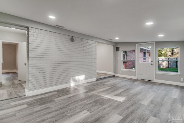 unfurnished living room with light hardwood / wood-style flooring, brick wall, and lofted ceiling