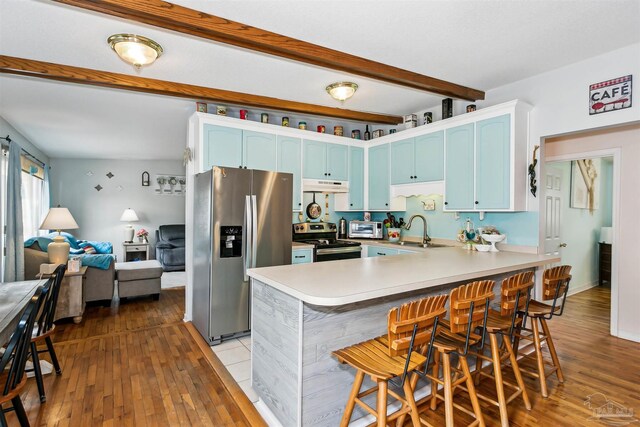 kitchen with under cabinet range hood, appliances with stainless steel finishes, a sink, beam ceiling, and a peninsula