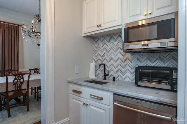 kitchen featuring white cabinetry, a chandelier, a sink, stainless steel appliances, and decorative backsplash