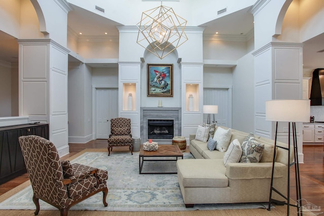 living room with a notable chandelier, hardwood / wood-style flooring, crown molding, decorative columns, and a towering ceiling