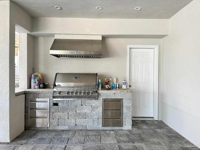 kitchen featuring stone finish flooring, wall chimney exhaust hood, and a textured ceiling