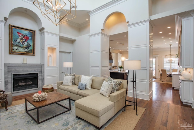 living area featuring a towering ceiling, ornamental molding, a high end fireplace, dark wood-style floors, and a notable chandelier