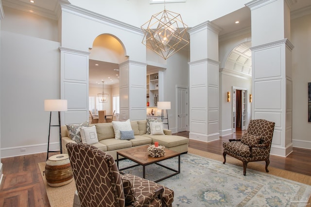 living room with a chandelier, ornate columns, a high ceiling, and wood finished floors