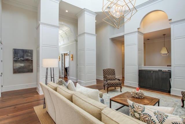 living area with crown molding, a high ceiling, decorative columns, and wood finished floors