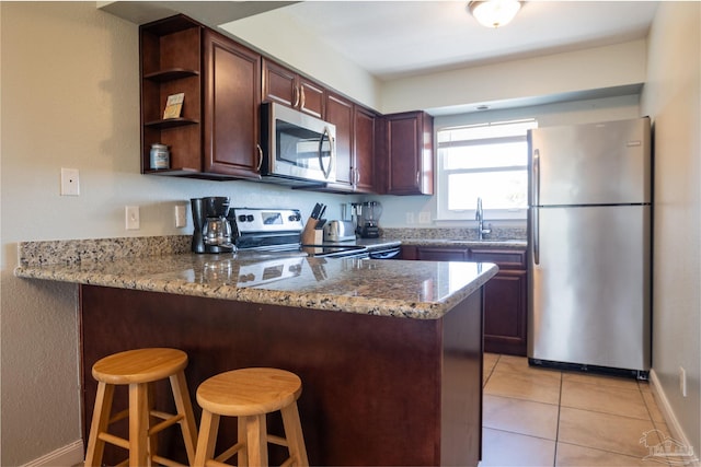 kitchen featuring light stone counters, stainless steel appliances, kitchen peninsula, and a breakfast bar