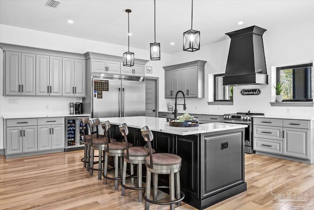 kitchen with custom exhaust hood, wine cooler, light wood finished floors, gray cabinetry, and stainless steel appliances