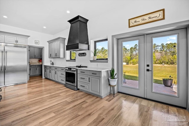 kitchen featuring premium range hood, light countertops, gray cabinetry, light wood-style floors, and appliances with stainless steel finishes